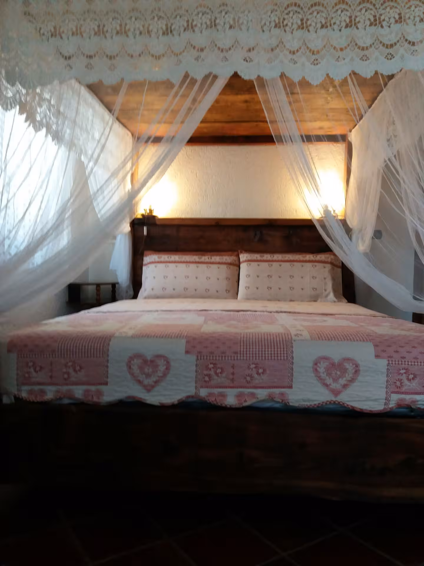 Canopy bed close-up with white lace draping, wooden beam ceiling and pink heart bedding